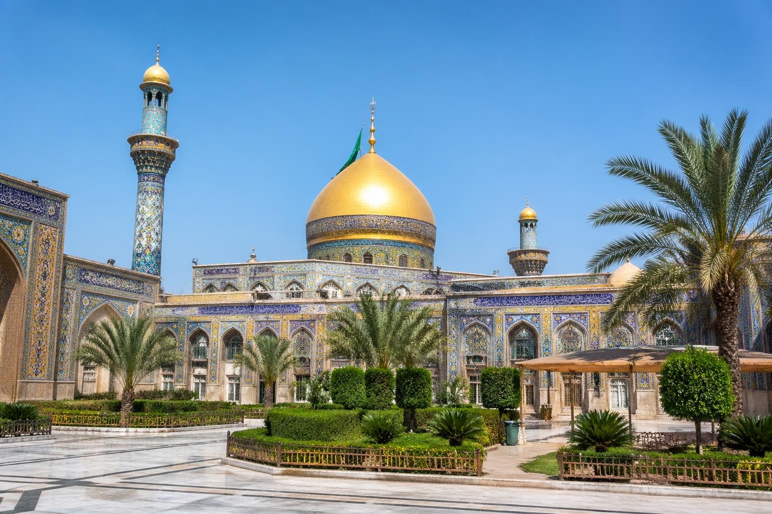 The Al-Askari Shrine in Samarra with its golden dome, minarets, and surrounding courtyard under a clear blue sky.